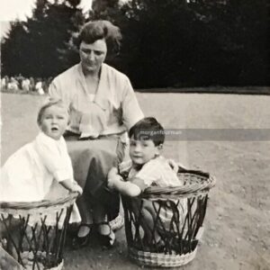 A mother crouches with two young children. The boys are playing inside wicker baskets.