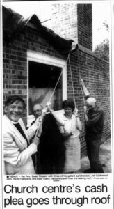 A smiling reverend and parishioners holding down a tarp draped over a roof.