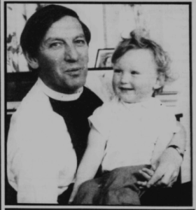 Ewen, in his reverend's vestments, has a smiling baby on his lap.