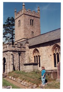 A girl in a blue shirt stands in front of a large stone church.