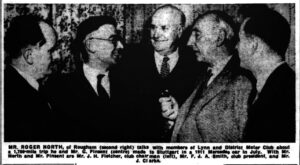 People crowd around a smiling man in glasses.