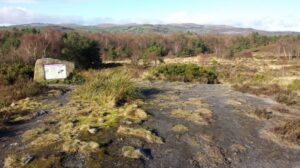 A scarred, muddy field , where a plaque is mounted on a large rock.