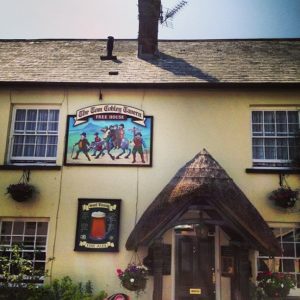 An old building with a colourful sign reading The Tom Cobley Tavern Free House near the door.
