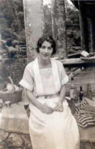 Betty sits in a simple, belted white dress.