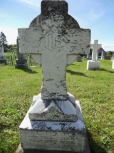 A modern photograph of a large, grey stone cross memorial. It is marred by black lichen.