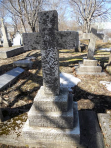 A lichen-encrusted, cross-shaped gravestone.