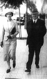 A well-dressed white couple walk down the street.