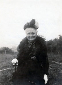 A black and white photograph of Lady Emily as an older woman, smiling with her cane. 
