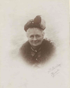 A smiling older woman in a hat and fur collar.