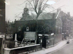 Faded black and white photograph of a stone building with a large sign out front.