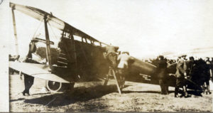 Faded black and white photograph of a man inspecting an old biplane.