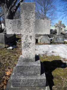 A lichen-crusted stone cross headstone.