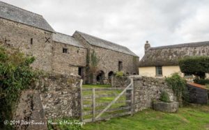 A photograph of an old stone farmhouse behind a low stone wall and a old wood gate.