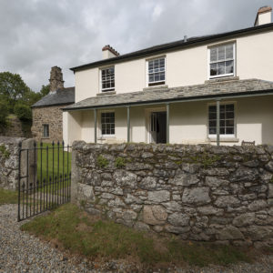 Modern photograph of a two story house behind a stone fence.