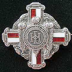 A silver cross brooch with red and white bands. It is engraved with a symbol and a Latin phrase.
