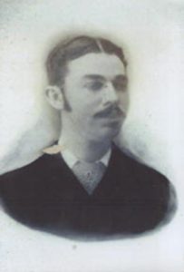 Faded black and white photograph of a white man with short dark hair and a mustache.