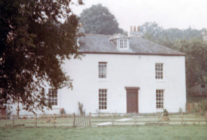 A washed out photograph of a large, simple house with a grey roof.