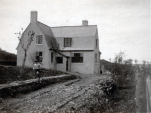 A young boy runs along a low wall in front of a country house.
