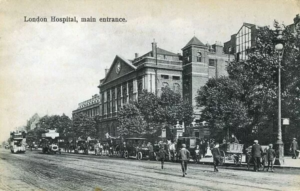 Black and white photo of a city street lined with 1920s cars. A huge, intimidating building appears behind it.