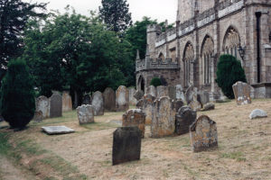 Photo of a lichen-covered, weathered graveyard in front of a stone church.