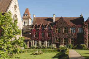 Modern photograph of a large, multi-storey building covered in thick red ivy.