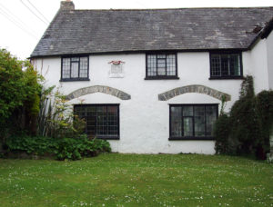 A two-storey white building with a simple grey roof. There is a small white plaque on its wall.