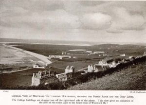 Greyscale photograph of a string of buildings against an attractive landscape.