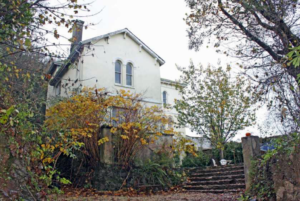 A white house shrouded behind trees.