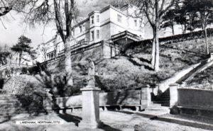 Black and white photo of a large white building on a hill. Down below, a sculpture sits in a courtyard.