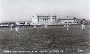 A large, attractive white building behind a field on which cricket is being played.