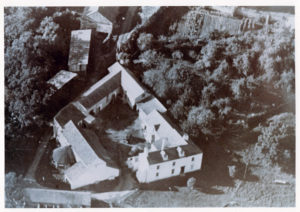 Cluster of large white building with dark roofs photographed from above.