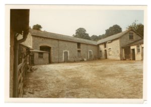 Faded photograph of an empty farmyard surrounded by grey stone farm buildings.