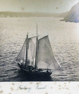 An old, mold-spotted black and white photograph of a fishing vessel with tall white sails.