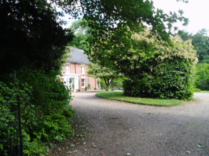 A large red building behind high green hedges.