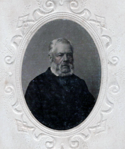 An older man with a large muttonchop beard.