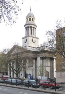 A white church building with stone columns and a towering spire.