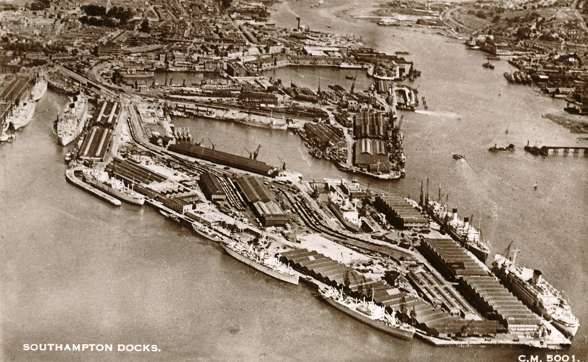 Black and white aerial photograph of the Southampton Docks. Peninsulas of construction jut out into the water.