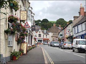 Modern photograph of a city street with white buildings and cars lined along one side.