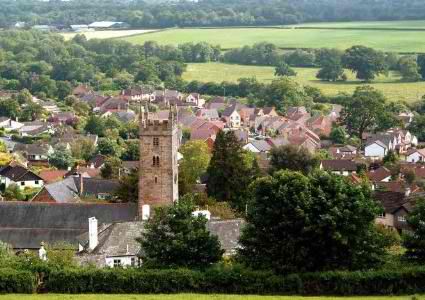Photograph of red and black roofs among trees. A tall church steeple stands in the center.