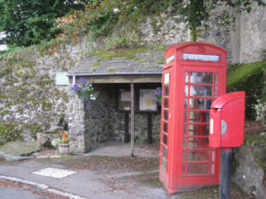 A red telephone box in front of a stone, covered bus stop.