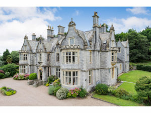 Attractive stately home in grey stone. It sits among well-tended gardens and trees.