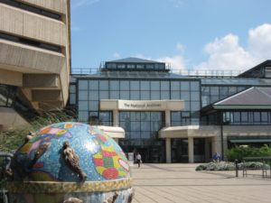 A glass-fronted building with a globe sculpture in the courtyard.